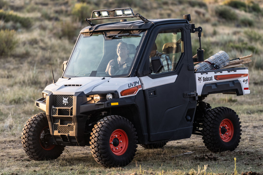 Two people transporting fence supplies in a Bobcat UV34 utility vehicle